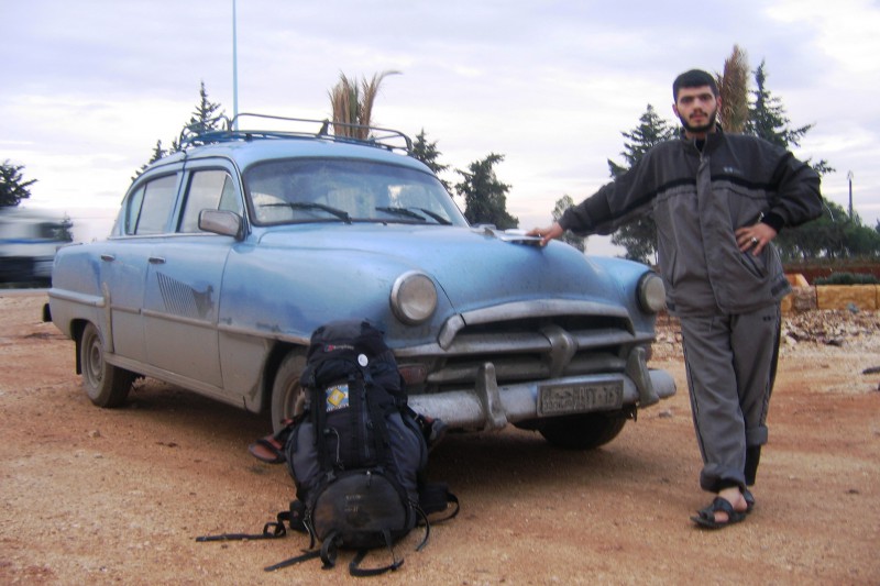 A blue old car, a man and a backpack
