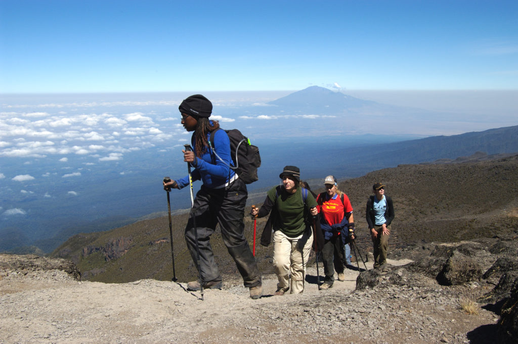 A guide in a blue jacket leads a group of trekkers up Mount Kilimanjaro