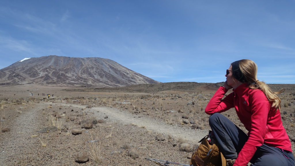 Sitting woman with blond hair looks along a trek to Mount Kilimanjaro