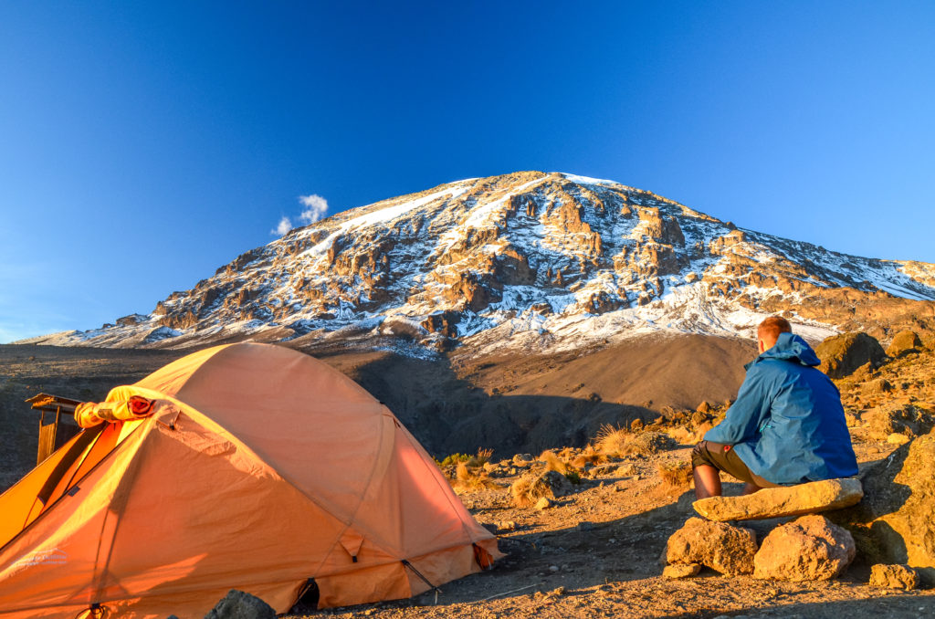 Man sits next to his tent at sunrise on Mount Kilimanjaro