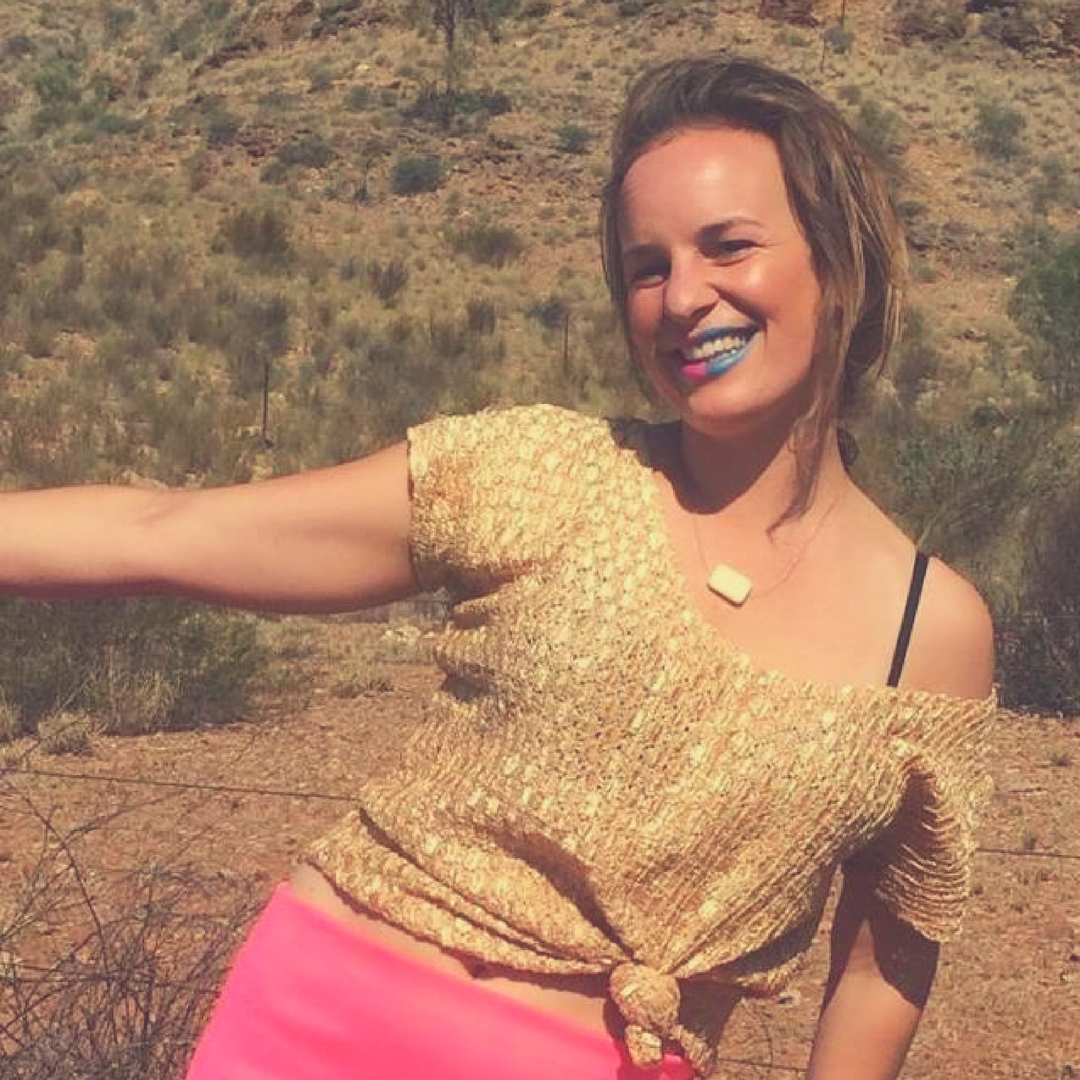 Smiling blonde woman with a gold shirt and blue and pink lipstick in the desert