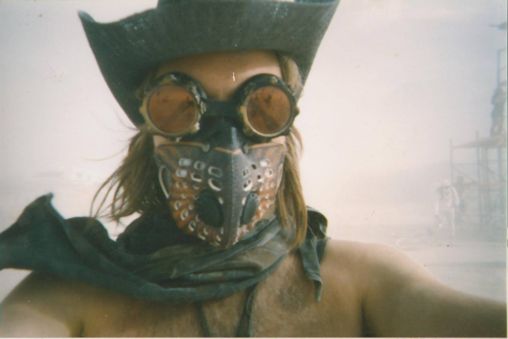 Selfie of a shirtless man with long hair, a mask, goggles and a cowboy hat in a dusty desert storm at Burning Man festival, Nevada