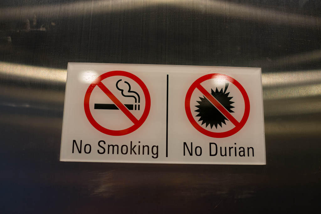 Two signs on a window, one that says "no smoking" and the other " no durian" weird laws in Southeast Asia