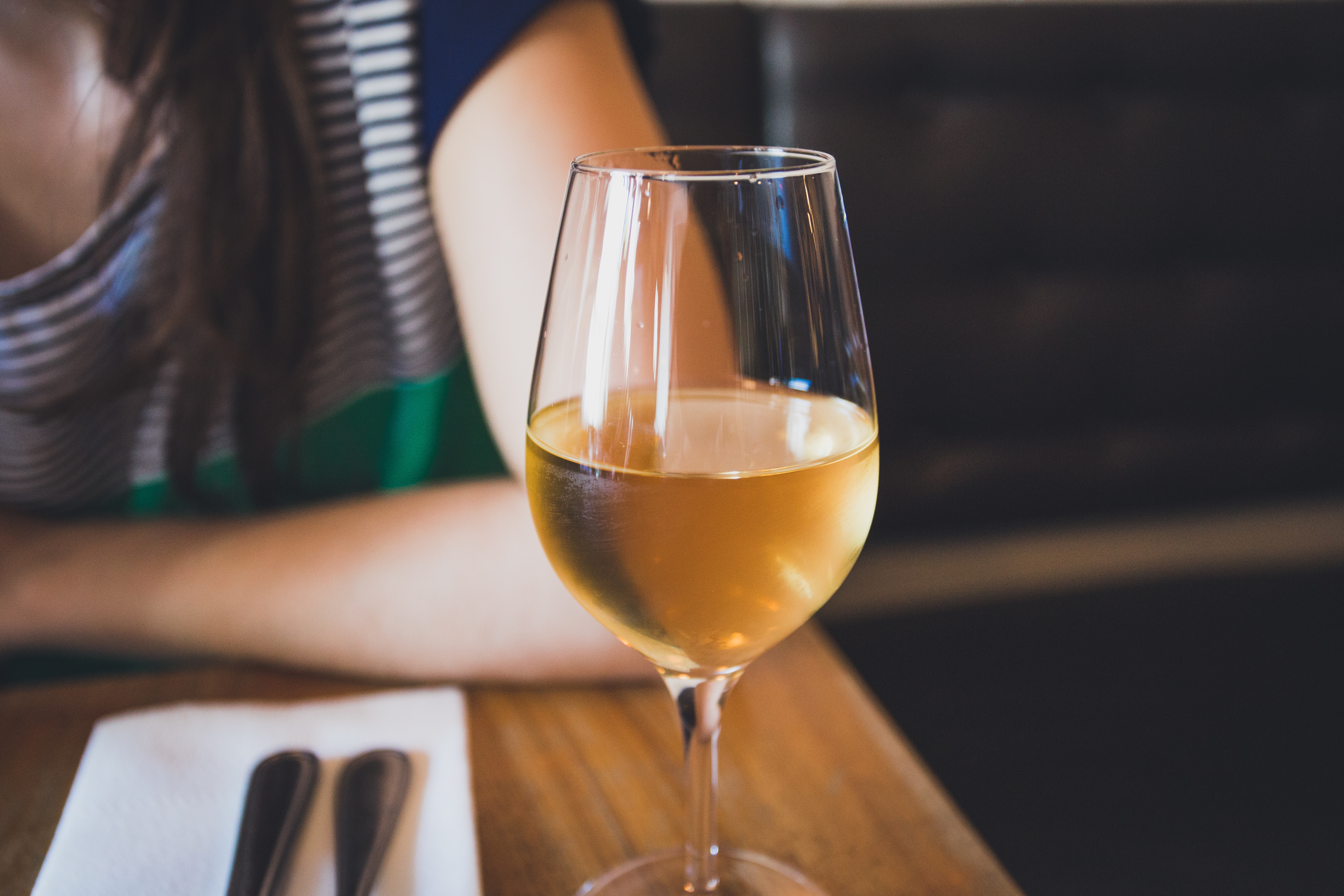 A woman's arm is visible, resting on a table behind a glass of chilled white wine. 