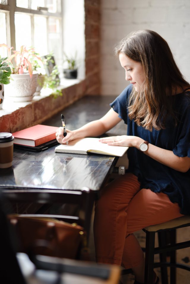 A young woman writing in a diary on a long wooden table